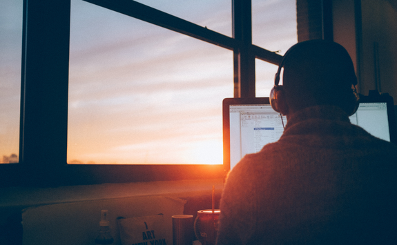 A person sits at their desk working as the sun goes down outside of the window